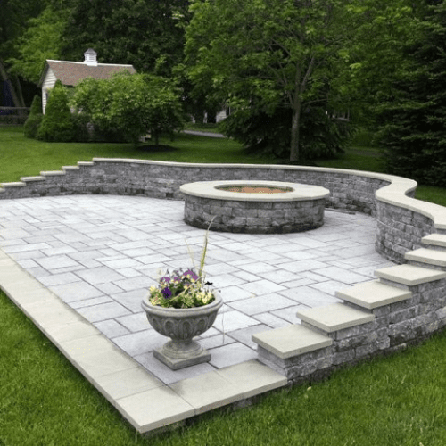 A uniquely built paver seating wall on top of a patio, with a paver fire pit in the center