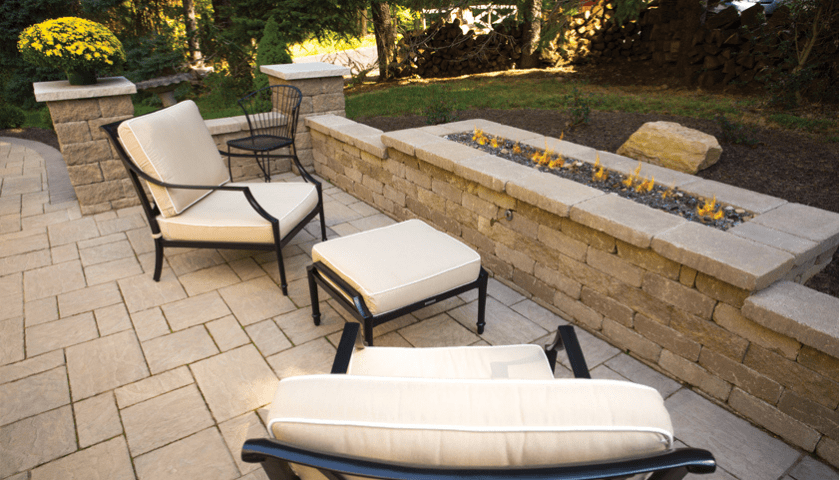 A beautiful white brick patio seating wall built next to a long fire pit on a backyard paver patio
