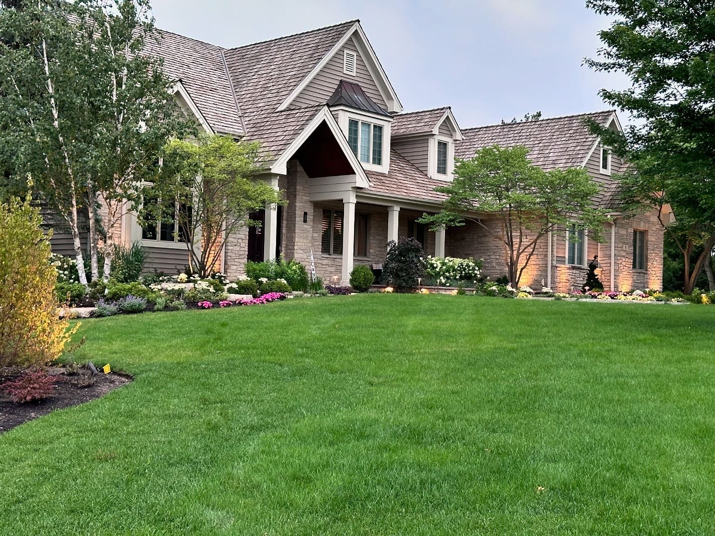 Elegant Front Yard Landscape with Lighting and Seasonal Plantings Front yard landscape design with manicured lawn, layered plantings, accent trees, and architectural lighting highlighting a stone home.