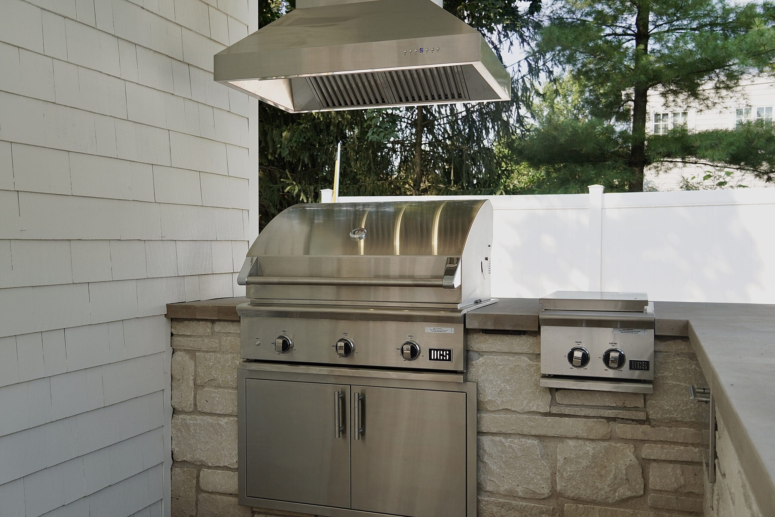 Luxury Outdoor Kitchen with Stainless Steel Grill and Ventilation Built-in outdoor kitchen with stainless steel grill, side burner, vent hood, and stone veneer base.