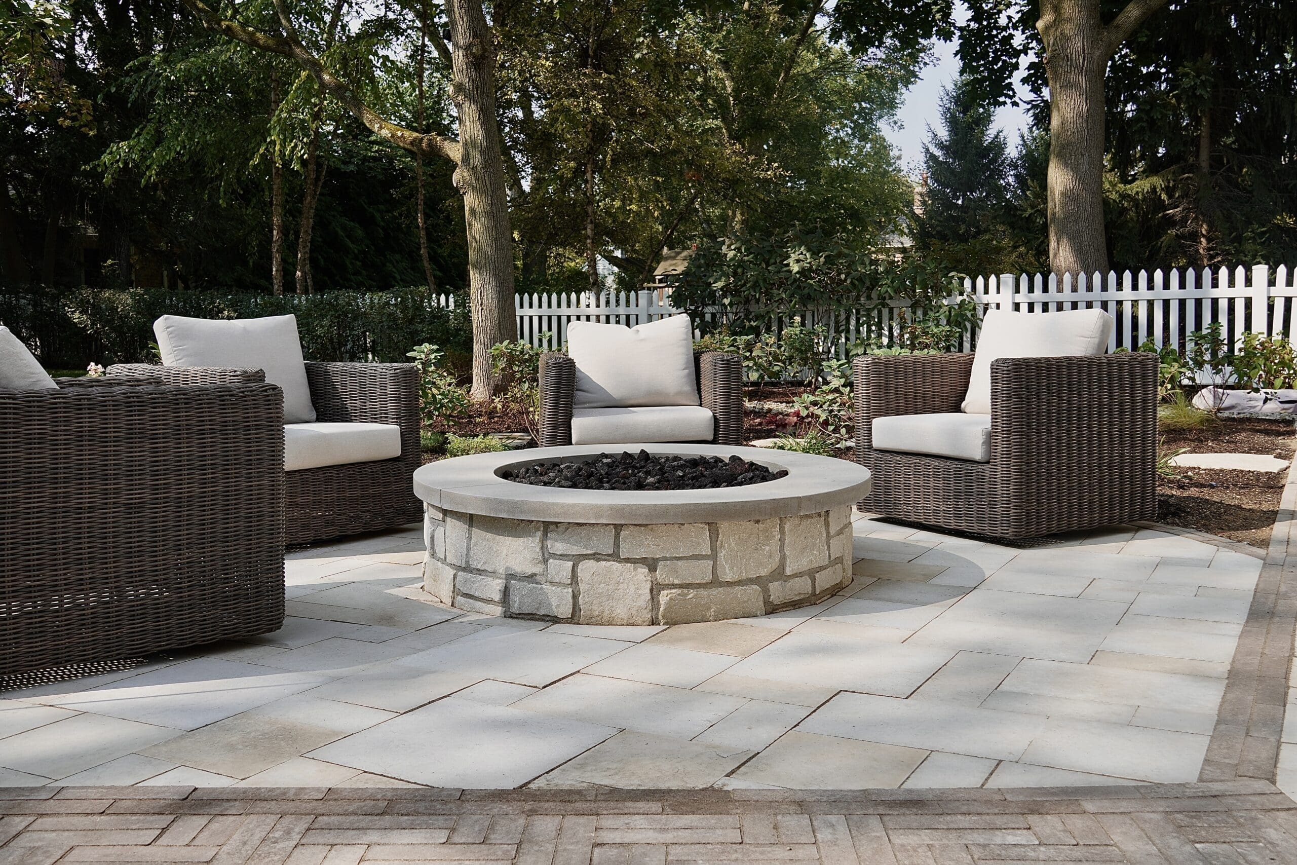 Custom paver patio with circular stone fire pit and lounge seating in a North Shore backyard.